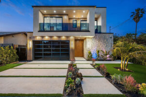 Modern two-story home with glass balcony, illuminated facade, landscaped front yard, and stylish driveway, highlighting premium home extensions and contemporary design.