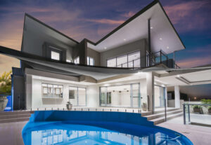 Modern luxury home with large glass windows, spacious balcony, and a curved swimming pool, showcasing premium home extensions and contemporary design