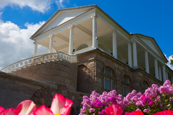 Elegant two-storey home with classic columns and balcony, surrounded by vibrant pink flowers, showcasing a potential second storey addition.