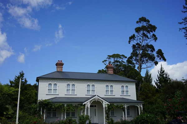 Classic two-storey Victorian-style home with grey roof, white façade, and ornate trim, surrounded by lush greenery and tall trees, perfect for a second storey addition.