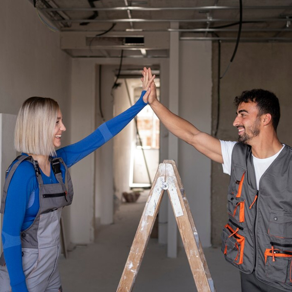 Two contractors celebrating with a high five during Home Renovations in a partially finished interior space with a ladder and exposed construction elements